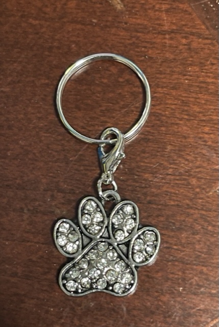 A small silver charm in the shape of a dog paw with bling in the sections of the paw.