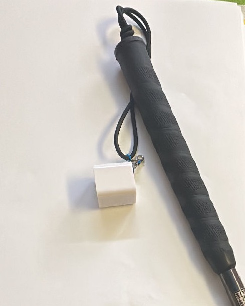 White, Cube-shaped, Deluxe Bluetooth Charm hanging from the wrist strap of a cane.