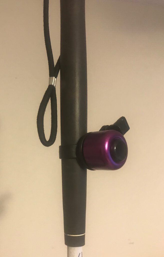 Purple mobility bell with black detailing. attached to the handle of a cane