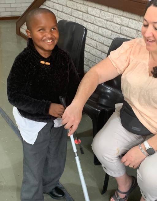 Smiling young student learns to use their new mobility cane with the help of a YCG volunteer.