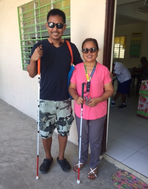 A man and woman smile outside a doorway with their new canes.