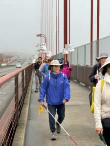 a group of people cross a bridge, walking with their canes and signs that read "I Cane Do Anything."