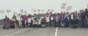 A large group of people pose against a foggy background on a road with canes and signs during their march for White Cane Awareness Day.