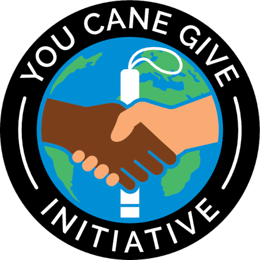 YCG logo consisting of a circular logo with a black border. Inside, there is a depiction of the Earth with the continents visible in green and the oceans in blue. Over the Earth, there are two hands shaking, one is light-skinned and the other is dark-skinned. The handshake is positioned over Africa and Europe. A white cane, symbolizing blindness, is integrated into the handshake as part of the light-skinned hand's wrist. Above the Earth and handshake, the text reads "YOU CANE GIVE INITIATIVE".