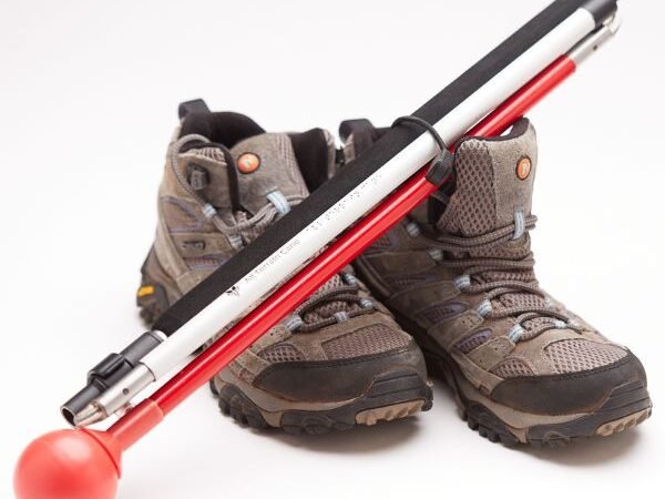 Folding All Terrain Mobility Cane propped up on hiking boots