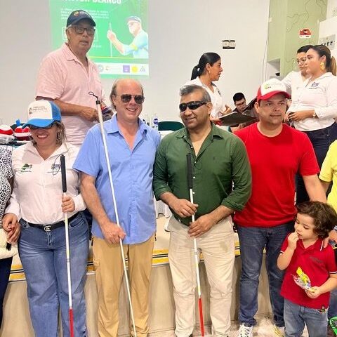 A YCG volunteer stands with a group of men, women and children in an auditorium. Each of them are smiling and holding canes