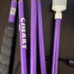 A vibrant purple cane with a shimmer finish, labeled "CHERRY" in bold white letters. It features a black grip and a white marshmallow-style tip, with a tag reading "Kustom Cane."