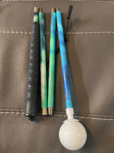 A beautifully designed mobility cane featuring a vibrant gradient inspired by the Northern Lights, with flowing shades of green, teal, and blue. It includes a black textured grip and a white rolling ball tip.