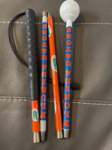 A cane wrapped in bright orange and blue designs with repeating "FLORIDA GATORS" text and Gators logos. It includes a black grip and a white rolling ball tip.
