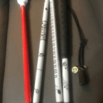 A musical-themed cane featuring segments wrapped in sheet music graphics, piano keys, and musical notes. The handle is black, and the tip is white with a red shaft segment leading into it. A small charm with a music note is attached.