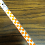 A cane with a white and orange checkerboard pattern, representing the University of Tennessee. It includes part of a Smokey (the dog) illustration near the top.